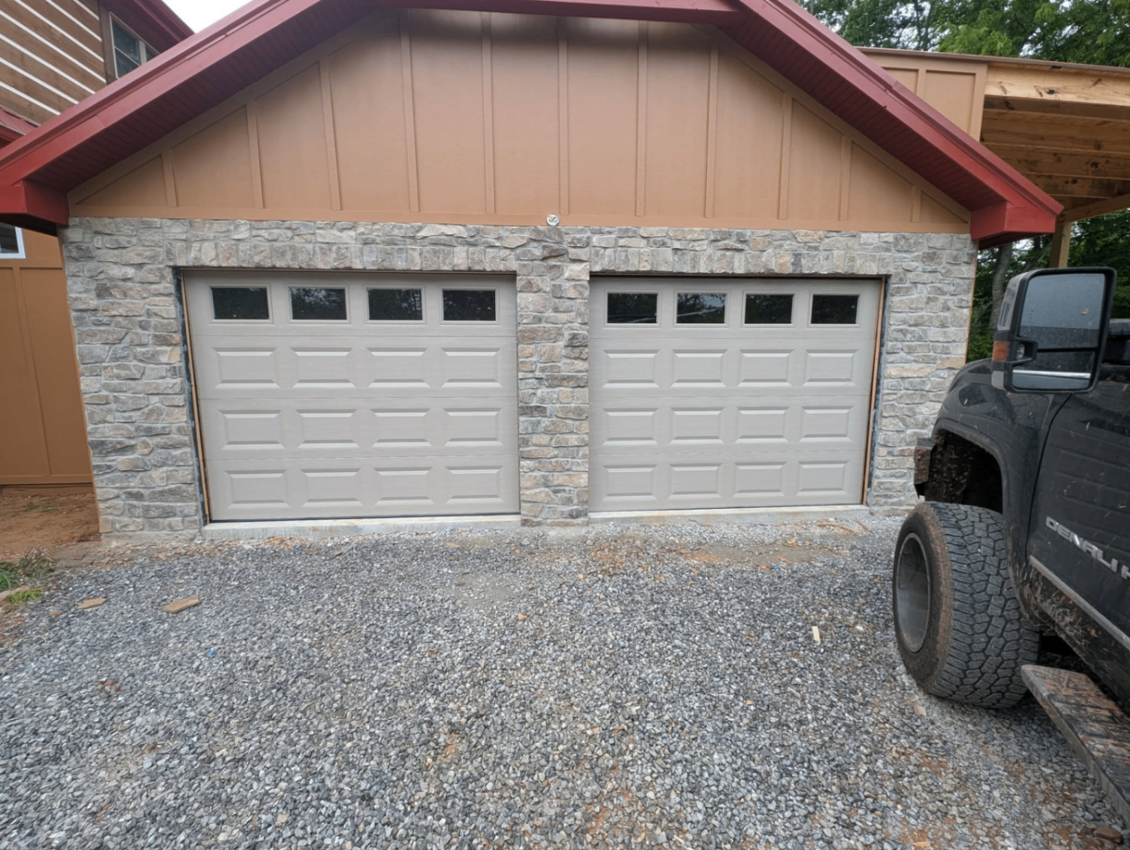 Two tan short-panel garage doors with windows on stone garage