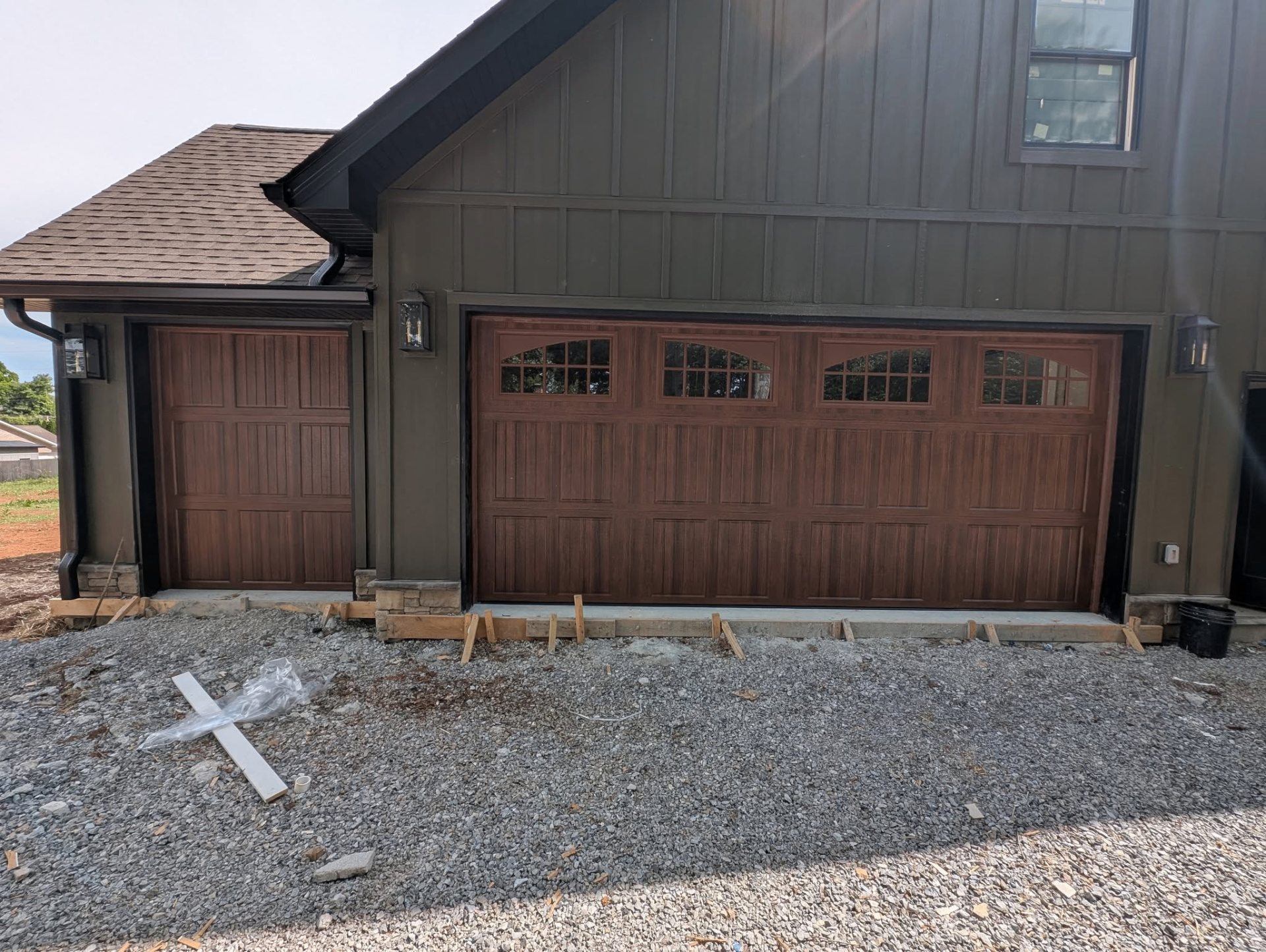 Woodgrain carriage-style garage doors with arched windows on dark green home